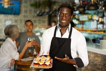 View on the African adult man holding tapas at a pub with diverse group in the background