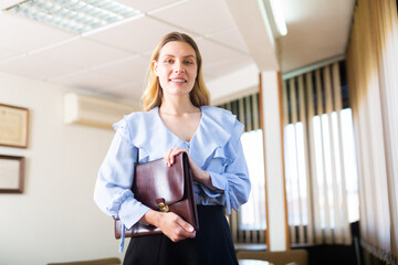 Smiling businesswoman standing in office with document case