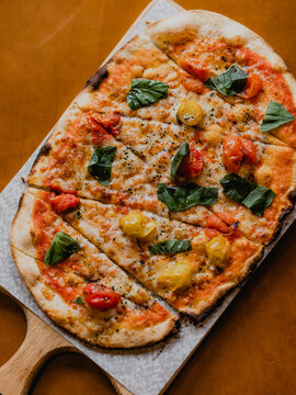 Vegetarian margarita pizza seen on a wooden board and ornage backdrop