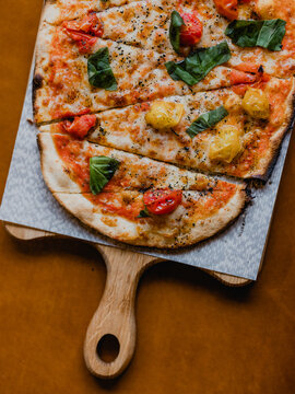 Vegetarian margarita pizza seen on a wooden board and ornage backdrop