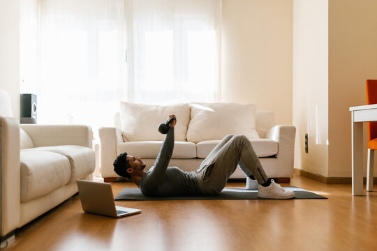 Sportsman exercising with kettlebells near laptop