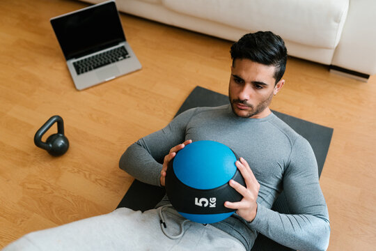 Athlete doing medicine ball crunches near laptop