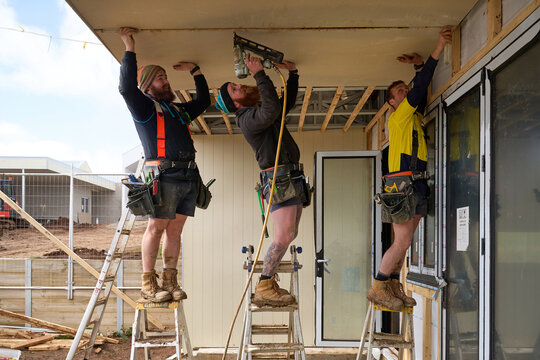 Tradies working as team to secure cladding board to roof
