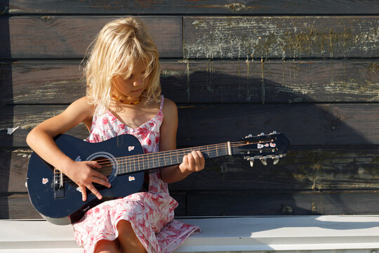 Girl playing guitar outside sunlit cottage