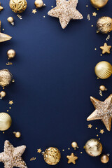 Luxury gold Christmas decorations on dark blue table. Elegant Christmas vertical banner design, poster, party invitation template. Frame of golden balls, stars, confetti. Top view.