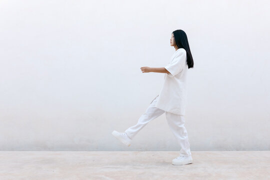 Stylish Asian woman walking near gray wall