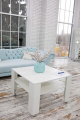 a table by the sofa with a decorative vase. room interior in blue and white colors