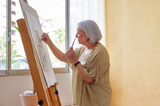 Focused senior artist drawing against window