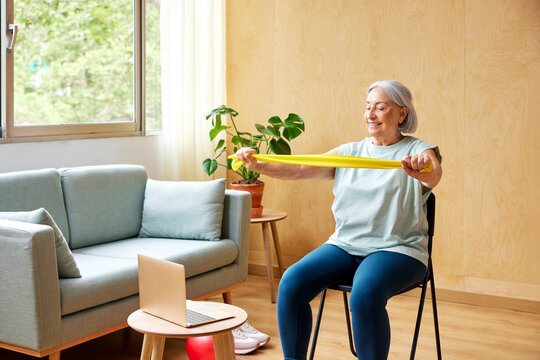 Senior woman exercising with elastic band near laptop
