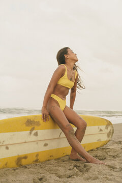 Asian Girl in bikini at the beach is sitting on a surfboard.