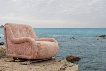 Fototapeta na wymiar An old armchair on the shore of the beach, surrealistic scenery.