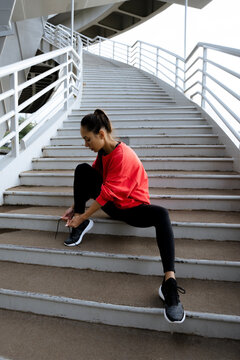 woman in sportswear tying shoe laces sitting on stairs outdoors