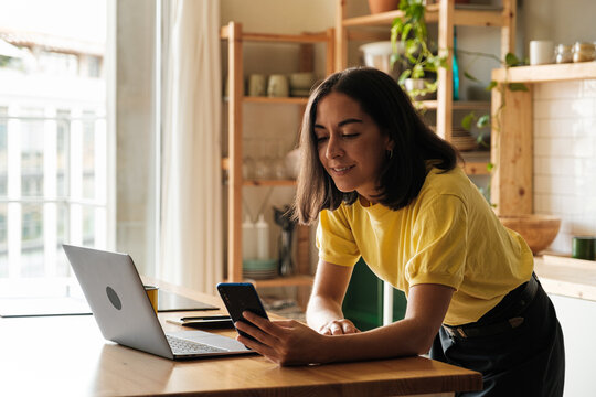 Woman browsing phone and laptop at home