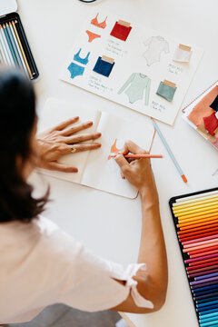 a dressmaker, colors a design on her notepad.