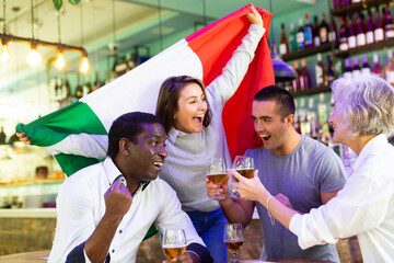 Excited diverse soccer supporters with flag of Italy celebrating victory with pint of beer in the...