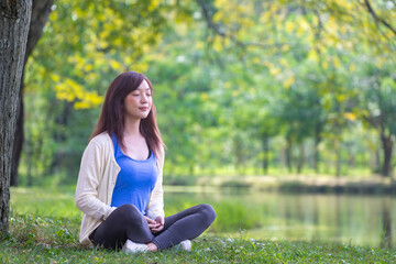 Woman relaxingly sitting and practicing meditation in the public park to attain happiness from inner peace wisdom under the tree in the summer