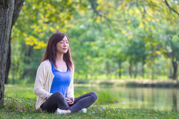 Woman relaxingly sitting and practicing meditation in the public park to attain happiness from...