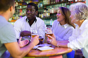 Company of multiracial friends drinking beer and talking with each other during the rest in a pub