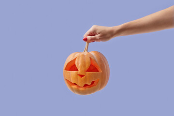 Halloween pumpkin with carved face held by woman.