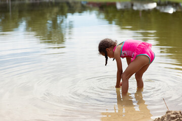 Young child bending over and playing in a lake