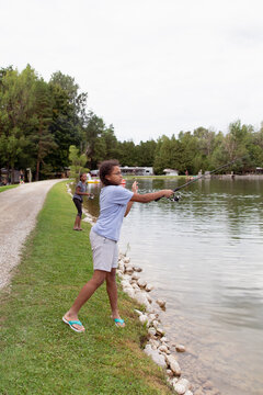 Teenager casting her fishing line as she stands next to a lake