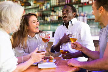Funny females and males with drinks celebrating together at beer pub. Focus on young woman