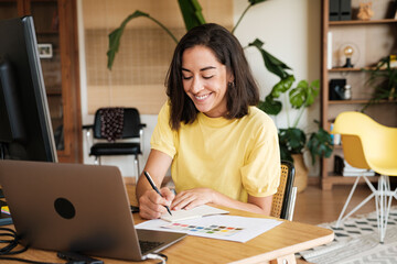 Woman taking notes while working on laptop