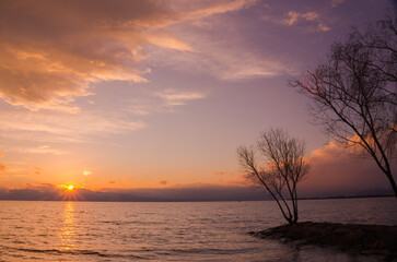 Fototapeta na wymiar 水平線に沈む夕陽とオレンジ色に染まった雲の風景
