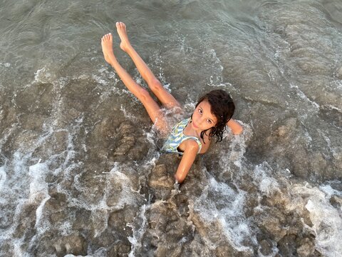 UGC kid in swimsuit dragged by waves on the seashore looking at camera