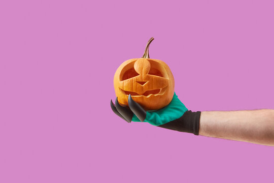 Jack-o-lantern in woman's hand in costume glove.