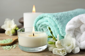 Beautiful composition with burning candles and different spa products on wooden table, closeup