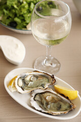 Plate of delicious raw oysters served with lemon and wine at wooden table