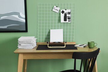 Typewriter, stack of papers and mood board on wooden table near pale green wall. Writer's workplace