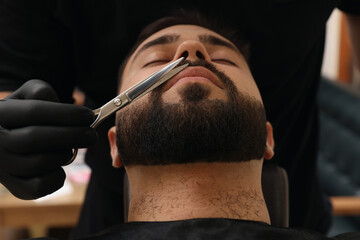 Professional hairdresser working with mustache of client in barbershop, closeup