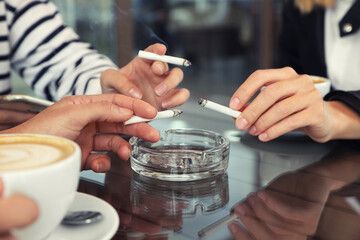 Fototapeta na wymiar Women holding cigarettes over glass ashtray at table, closeup