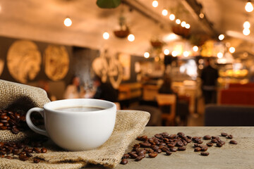 Cup of aromatic coffee and beans on wooden table in cafe, space for text