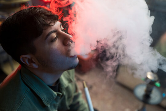 Young brunet exhaling hookah smoke