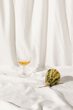 Green pumpkins on the white linen material. One glass and orange