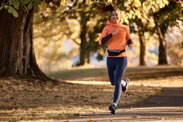 Poster Happy female athlete jogging on autumn day in nature. © Drazen