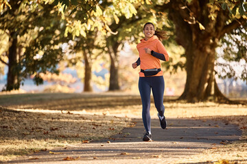 Young happy sportswoman running in park during autumn day.