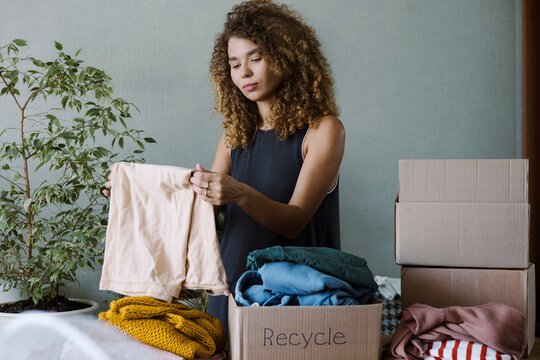 Curly young woman packing old clothes for recycling