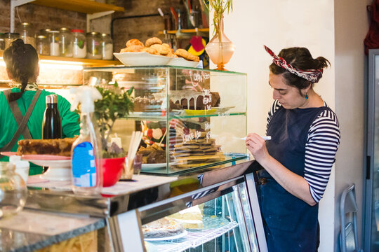 Business owner writing baked goods prices in showcase