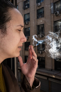 woman smokes tobacco at the window and throws the smoke outside
