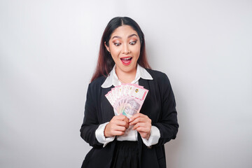 A happy young businesswoman is wearing black suit and holding cash money in Indonesian rupiah isolated by white background