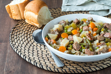 Close up of a bowl of homemade beef and barley stew, served with dinner buns.