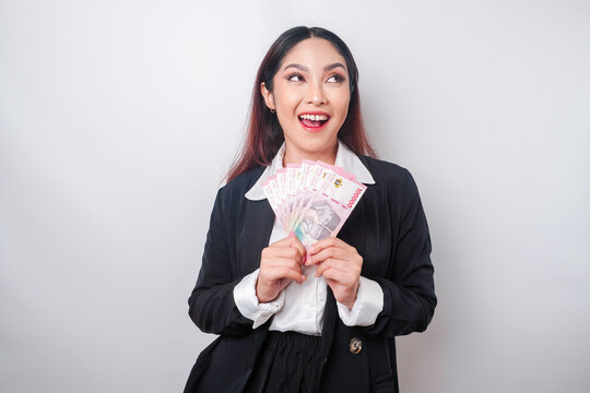 A thoughtful young woman is wearing black suit and holding cash money in Indonesian rupiah isolated by white background