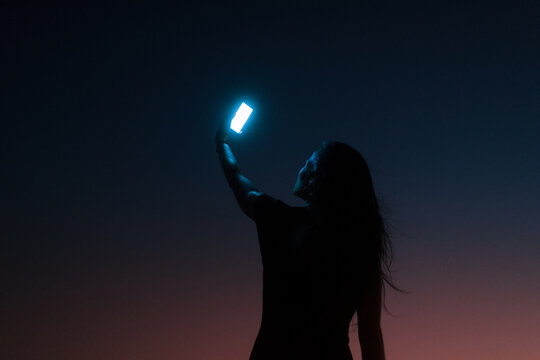 Woman silhouette holding up a bright mobile phone