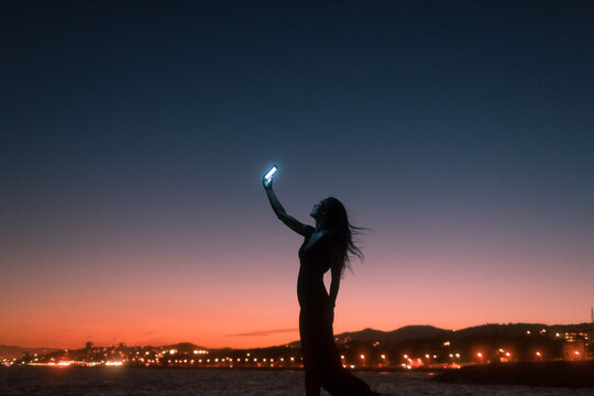 Woman silhouette holding bright smartphone