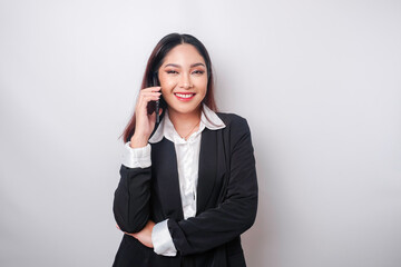 A portrait of a happy Asian businesswoman is smiling while talking on phone call wearing a black suit isolated by a white background