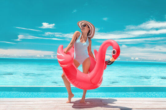 Travel Beach Vacation summer woman sunbathing relaxing with swimming pool pink flamingo float - funny luxury holiday travel concept woman in bathing suit and sunglasses on perfect sunny destination